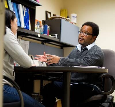 A faculty member advises a student at his desk.
